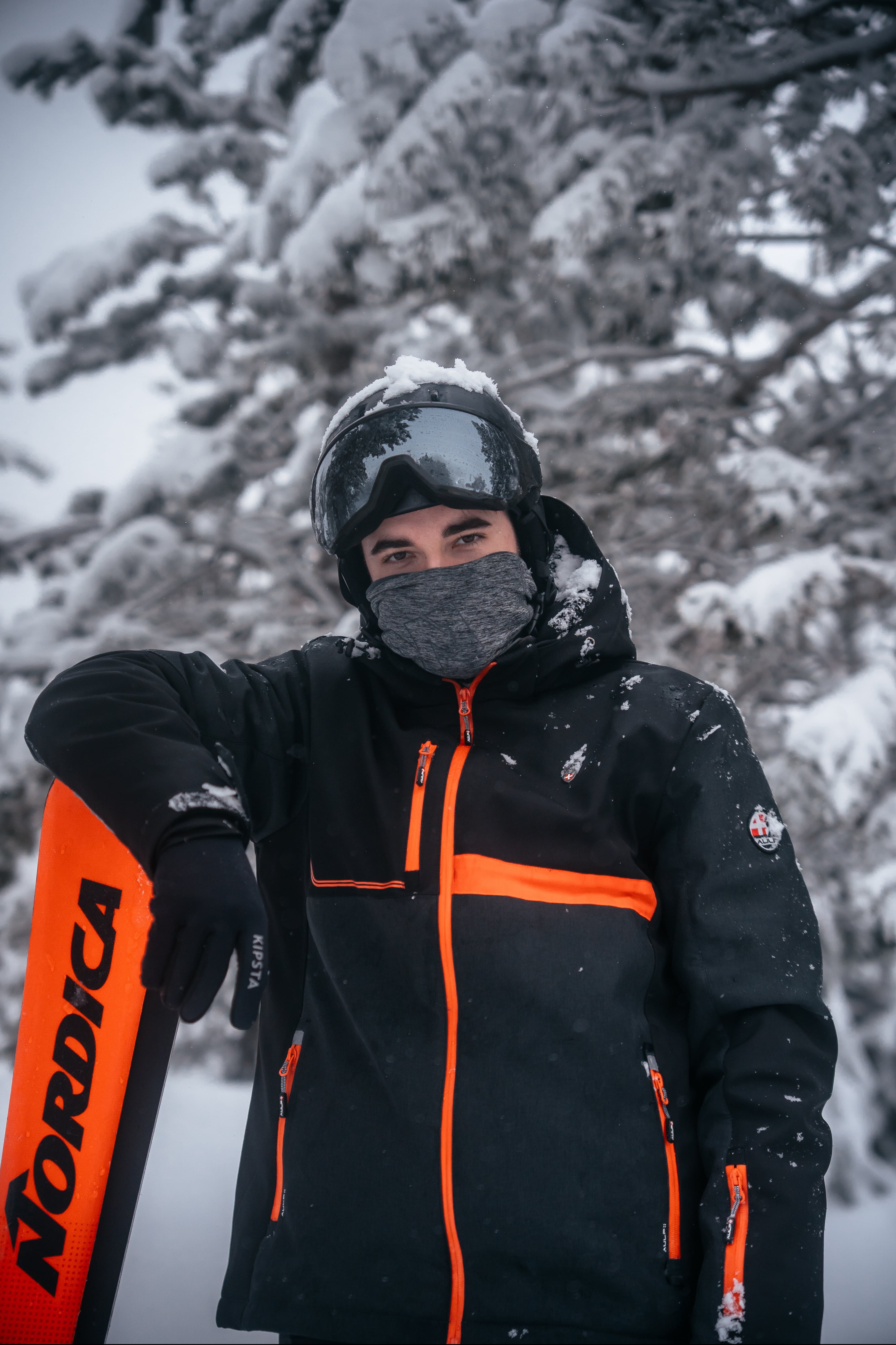 Skieur en tenue noire portant un ski orange dans une forêt enneigée